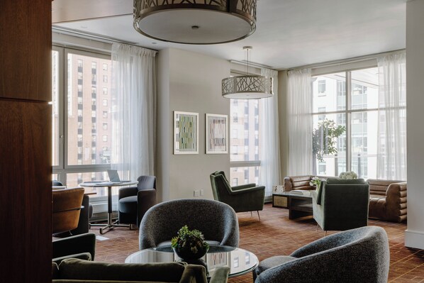 Uma sala de estar moderna com uma mesa de centro redonda de vidro, assentos confortáveis e grandes janelas com vista para a cidade.