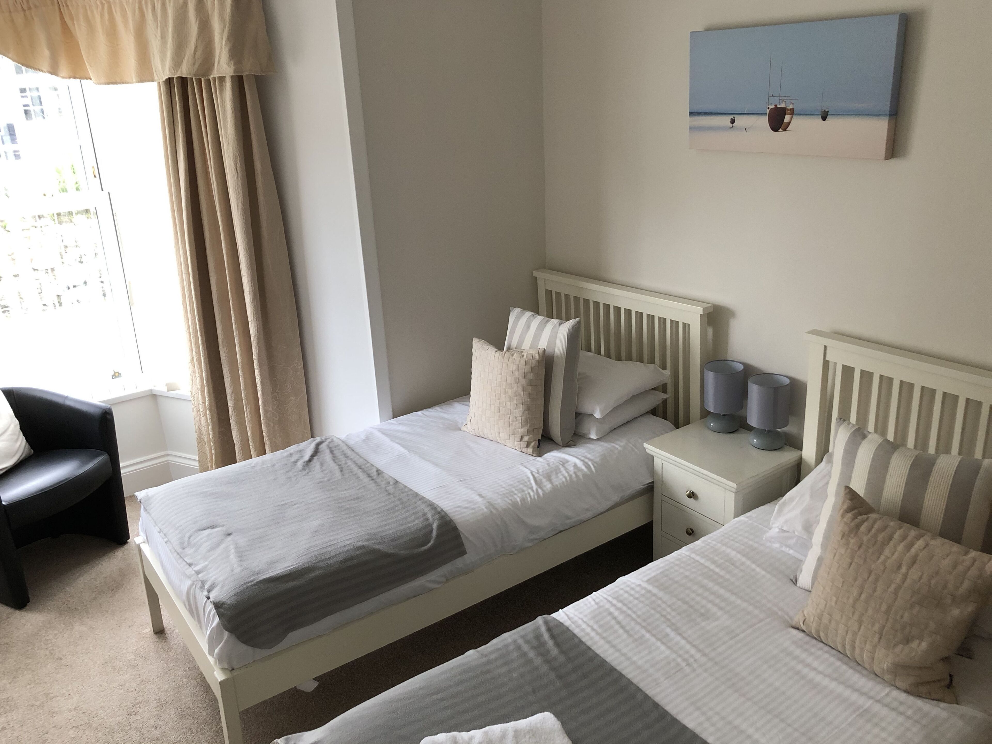 Une chambre d’hôtel avec deux lits, une table de chevet, une lampe, une chaise et un tableau au mur.