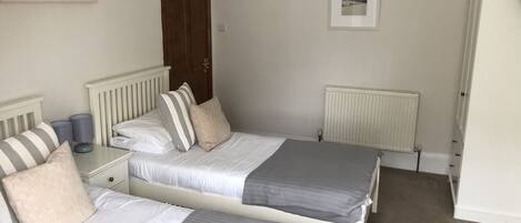 A bedroom with two beds, a white radiator, a door, and a framed picture on the wall.