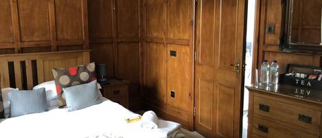 A bedroom with a large bed, wooden wardrobe, bedside table, and a dresser with a tea box.