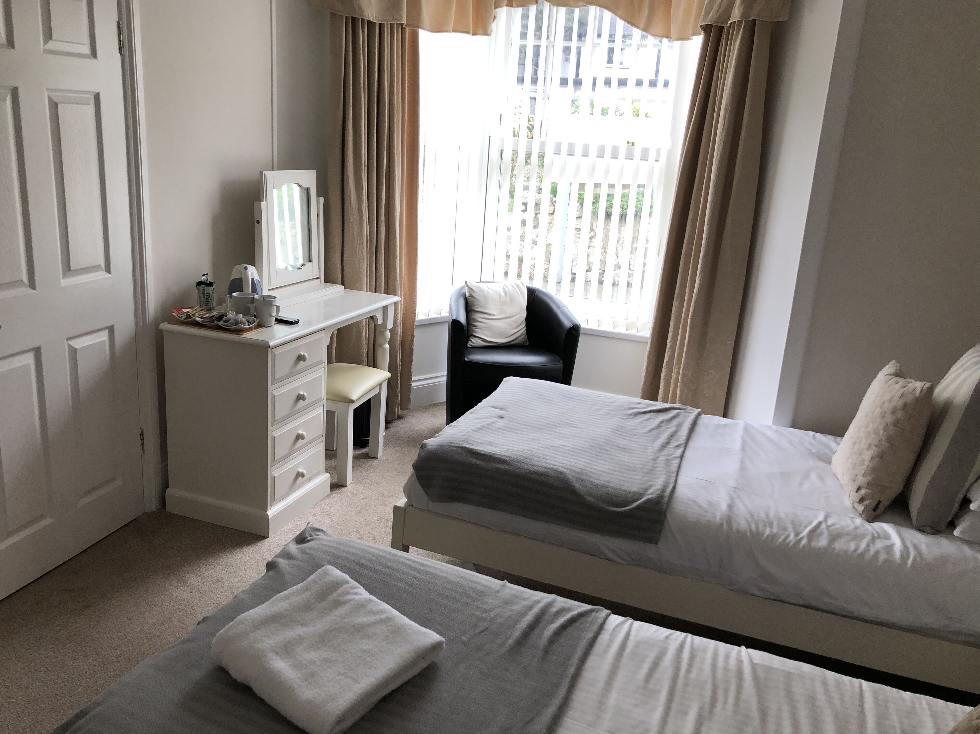 Une chambre d’hôtel avec deux lits, un bureau avec une chaise, un miroir et une fenêtre avec des rideaux.