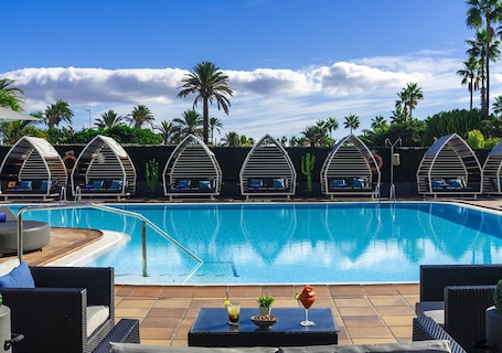 Una piscina al aire libre, sombrillas, sillones reclinables de piscina