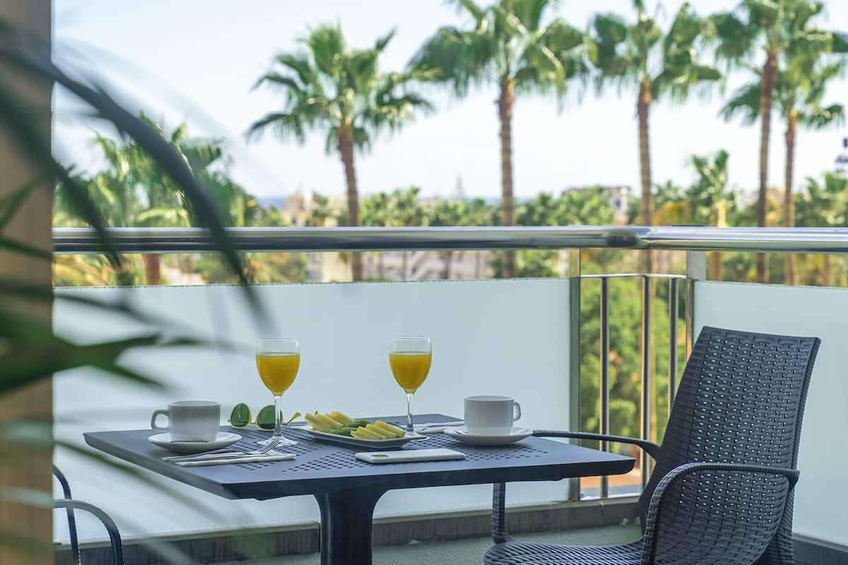 Ein Balkon mit einem Frühstückstisch, komplett mit zwei Tassen, einer Fruchtplatte und zwei Gläsern Orangensaft.