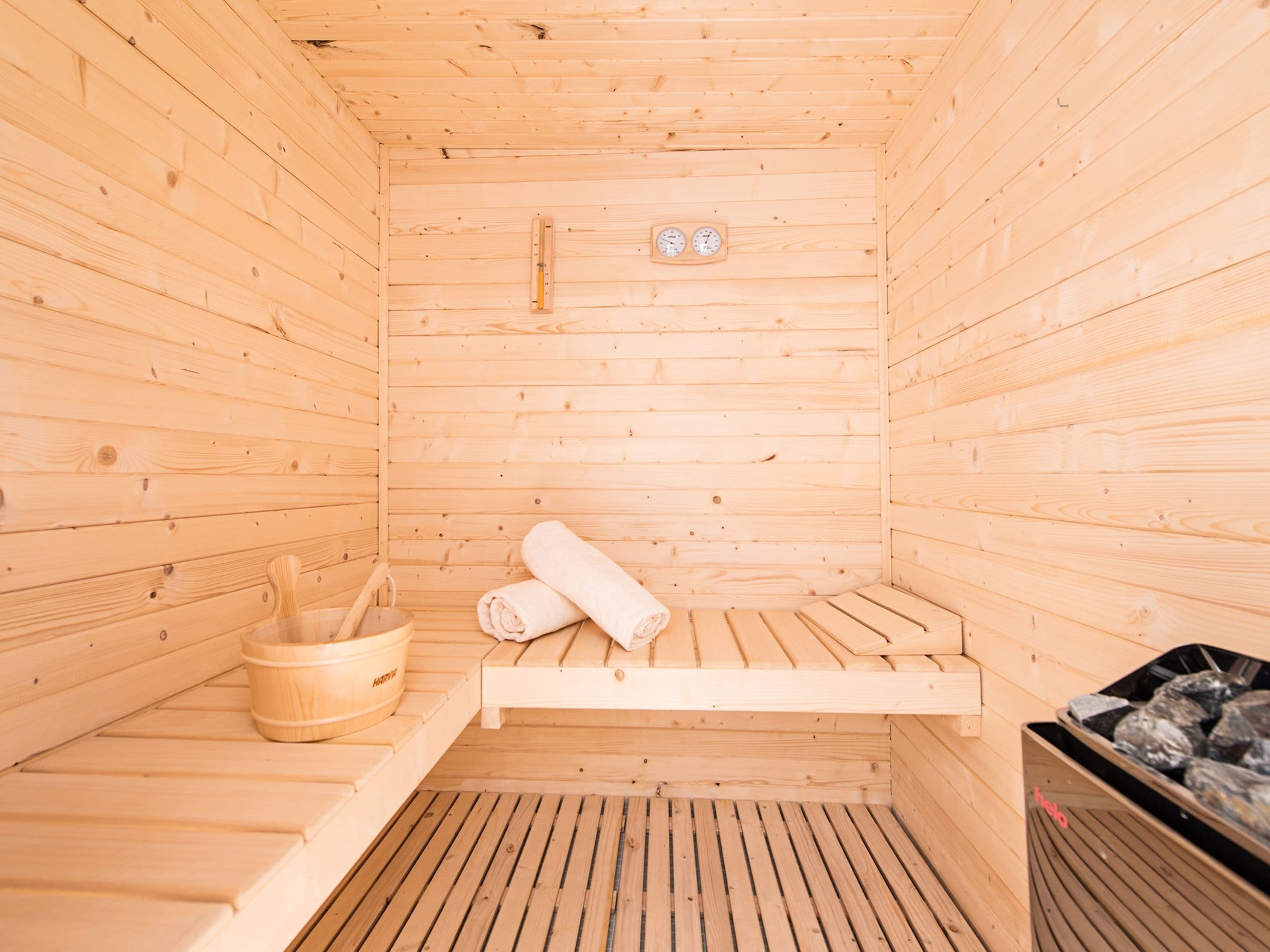 A wooden sauna with benches, a wooden bucket, and a trash bin.