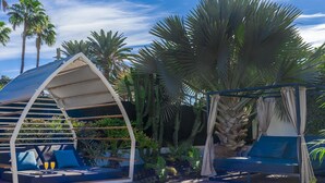 Un área de estar al aire libre de estilo moderno con techo curvo, asientos acolchados en azul y una pequeña mesa con bebidas.
