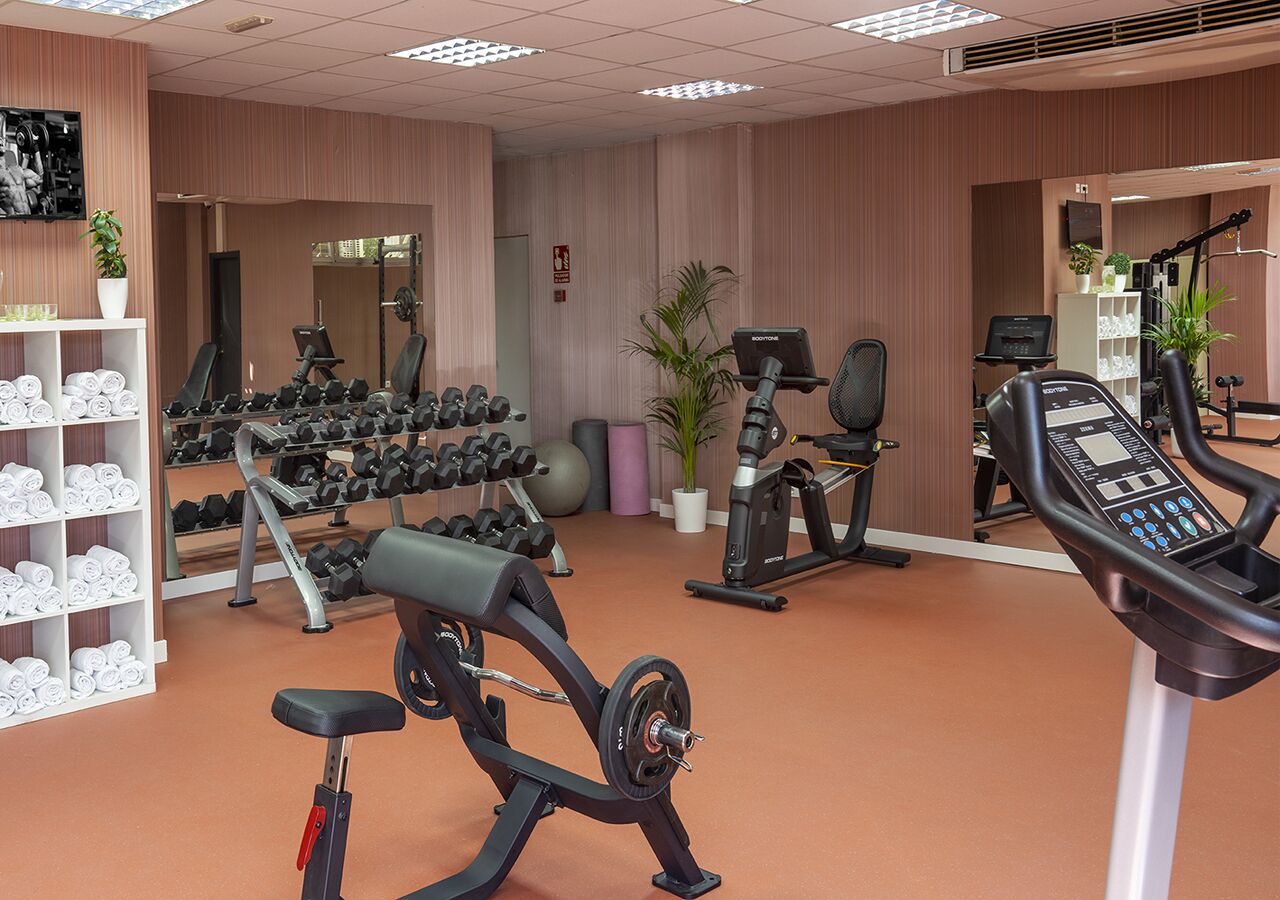 Un gimnasio con equipo de ejercicio, un espejo y un estante con toallas dobladas.