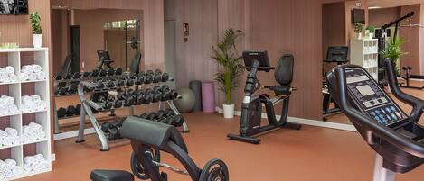 A gym with exercise equipment, a mirror, and a shelf with folded towels.