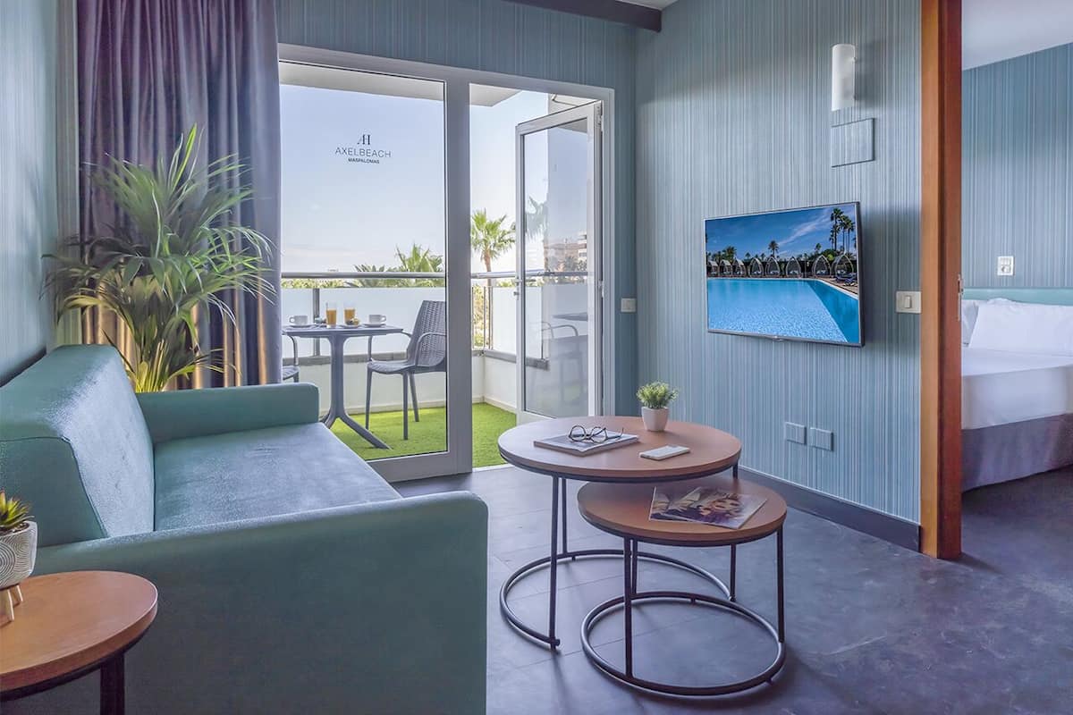 Ein Hotelzimmer mit einer Couch, zwei kleinen Tischen, einem Fernseher und einem Balkon mit Blick auf einen Pool.