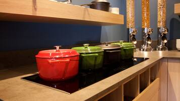 A kitchen with a black stovetop, wooden cabinets, and a shelf with pots and a kettle.