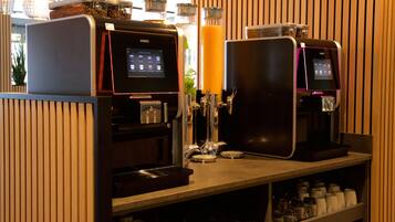 A coffee station with two espresso machines, a juice dispenser, and a variety of coffee cups and mugs.