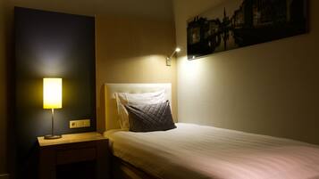 A neatly made bed with a pillow and a bedside lamp in a hotel room.