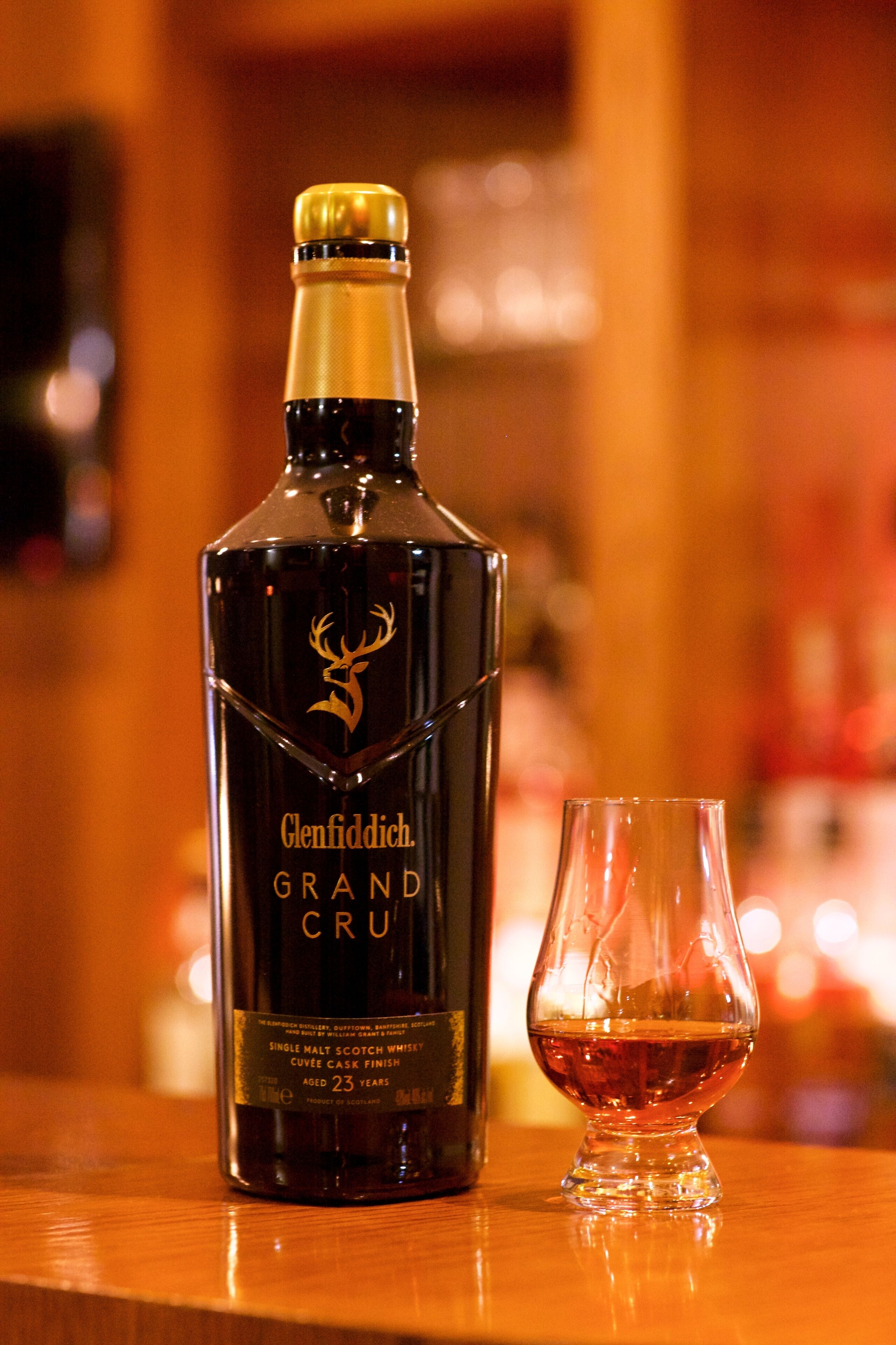 Una botella de whisky Glenfiddich Grand Cru y una copa sobre una superficie de madera.