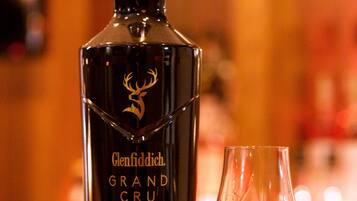 Una botella de whisky Glenfiddich Grand Cru y una copa sobre una superficie de madera.