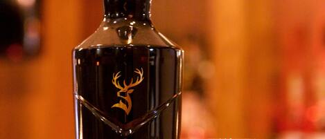 Una botella de whisky Glenfiddich Grand Cru y una copa sobre una superficie de madera.
