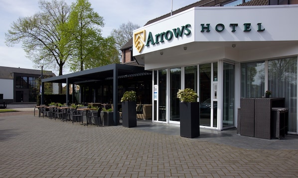 A hotel entrance with outdoor seating and a covered patio area. - Hotel Arrows (Uden)