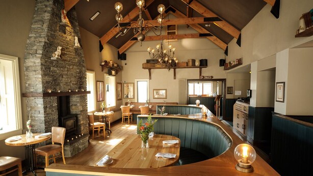 A restaurant with a stone fireplace, wooden ceiling beams, and a curved bar area. - Hotel Doolin (Doolin)