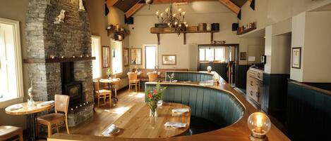 A restaurant with a stone fireplace, wooden ceiling beams, and a curved bar area.