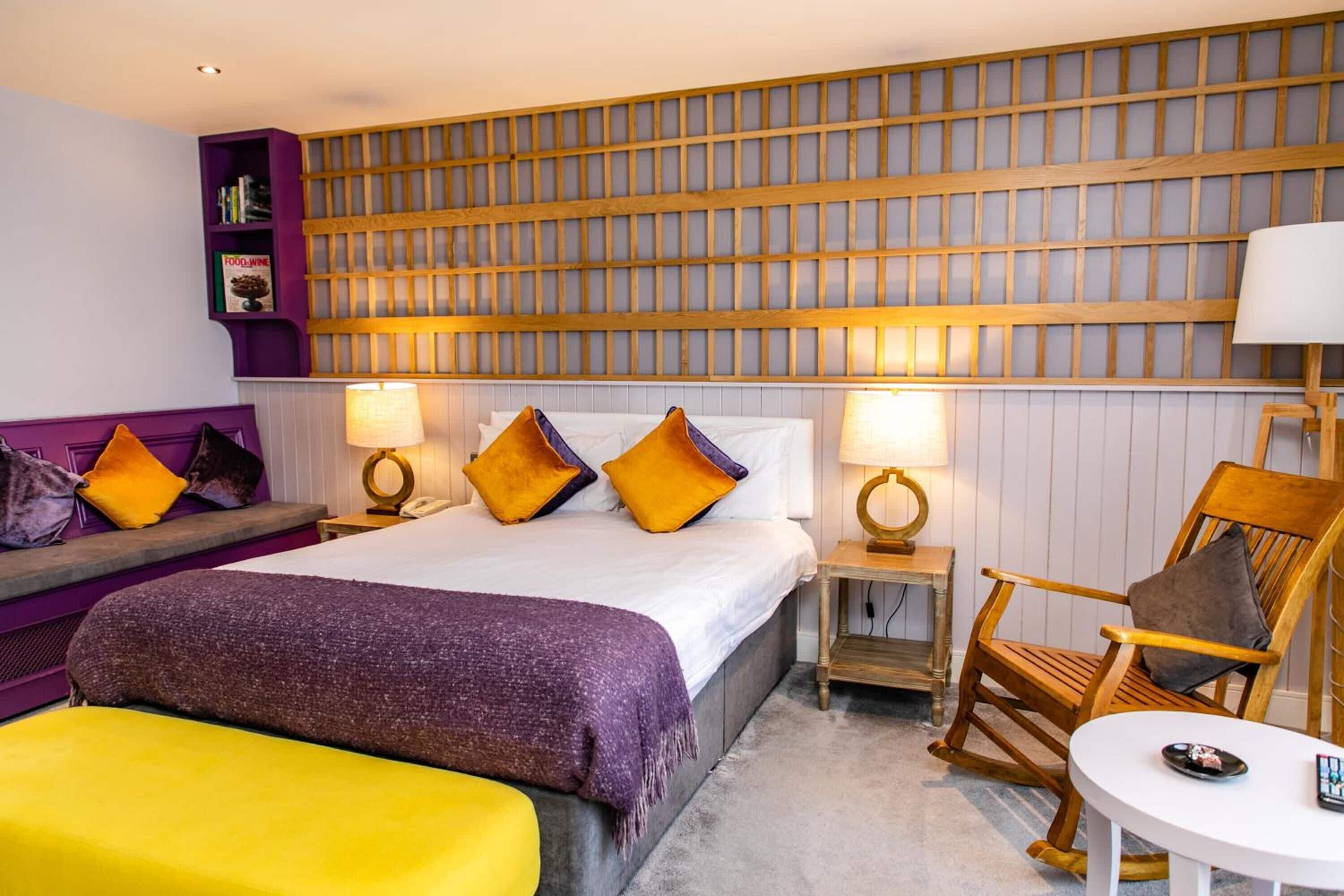 A hotel room with a bed, a seating area with a sofa and armchairs, a small table, and a wall with a wooden panel design.