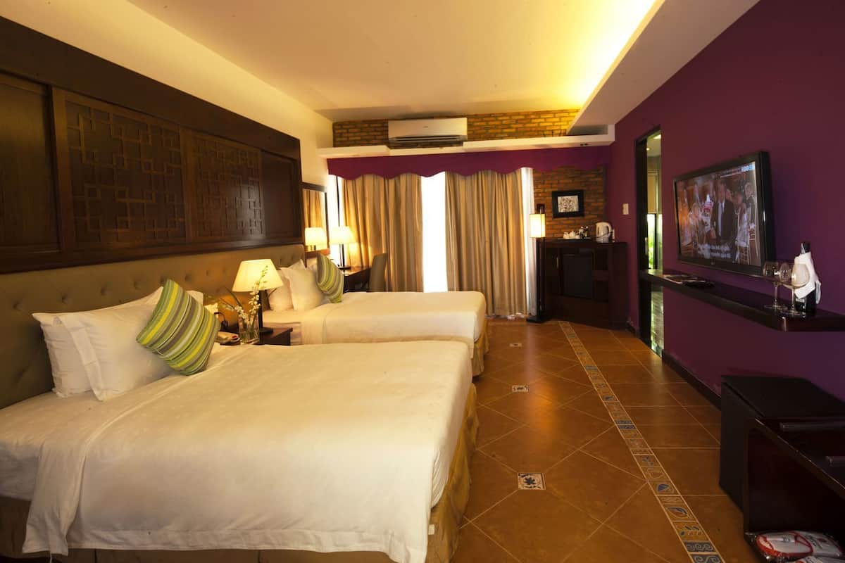 A hotel room with two beds, a TV, a desk, and a bathroom.