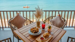 A wooden table with a plate of food, a drink, and a decorative vase on a balcony overlooking the sea.