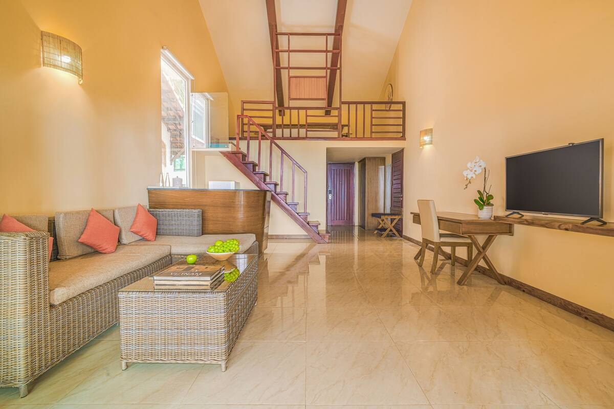 A spacious living area with a sofa, coffee table, and a TV. A staircase leads to an upper level.