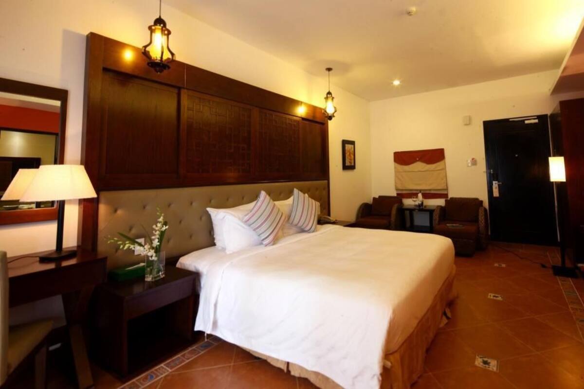 A hotel room with a large bed, a nightstand with a lamp, a chair, and a desk.