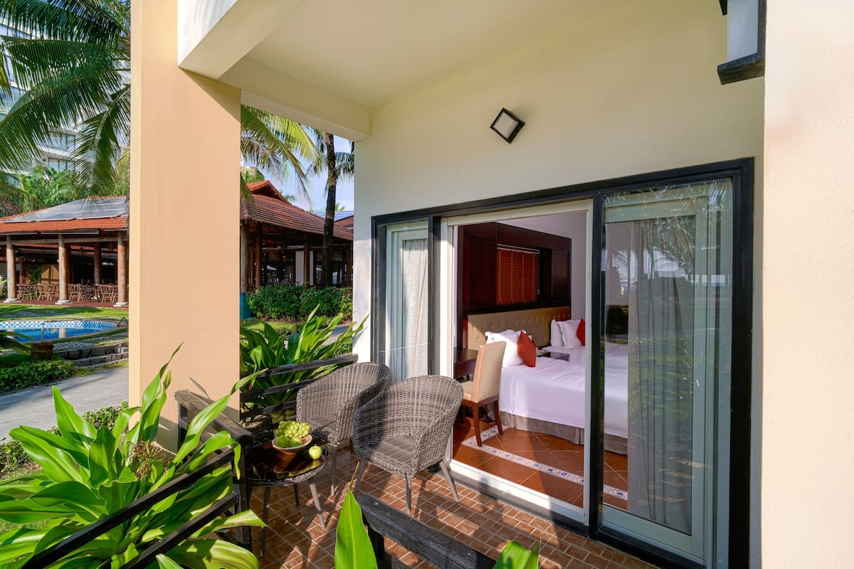 A hotel room with a large sliding glass door, a bed, a chair, and a small table with fruit.