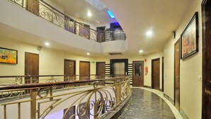 A hotel corridor with a curved marble floor, a metal railing, wooden doors, and a mezzanine level with a balcony. - Shanti Villa (New Delhi)