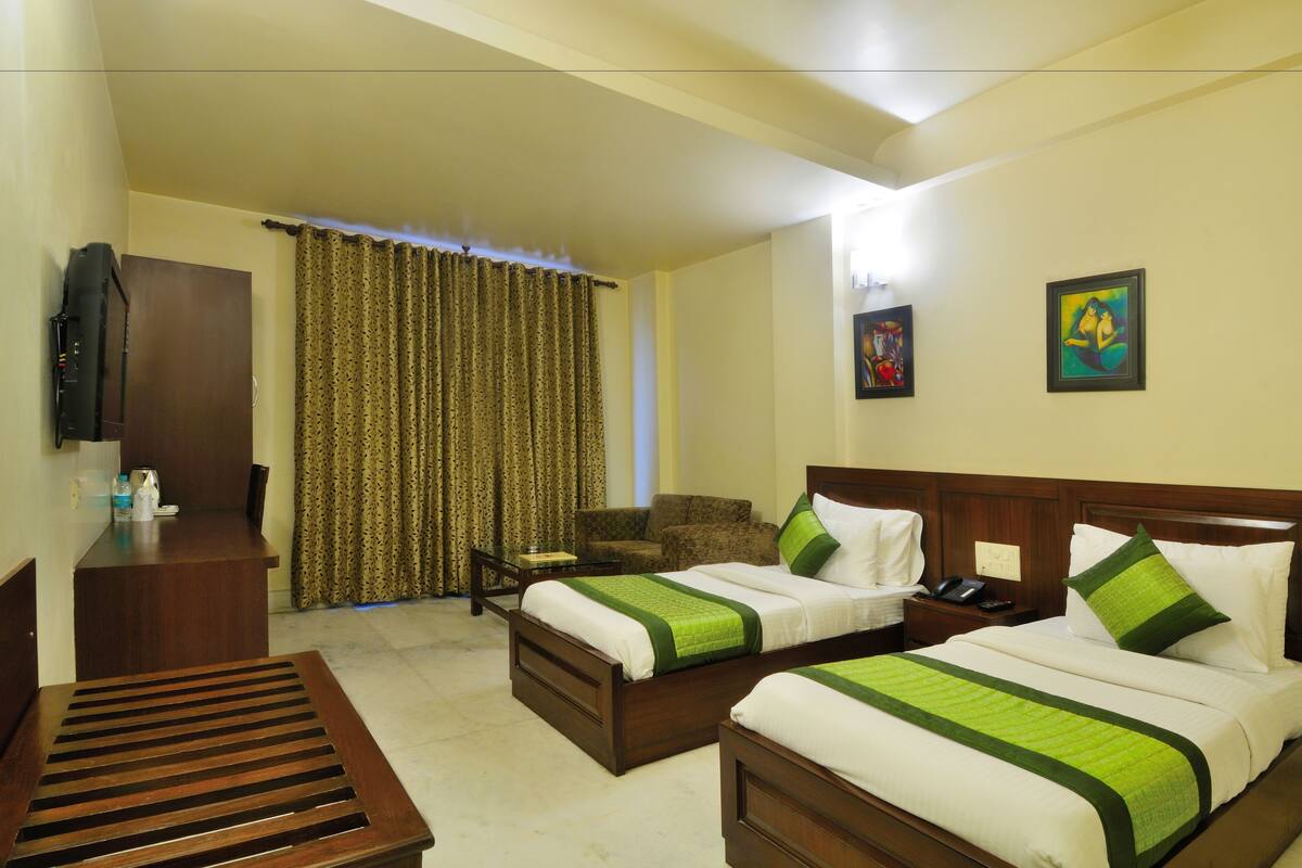 A hotel room with two beds, a desk, a chair, a TV, and two paintings on the wall.