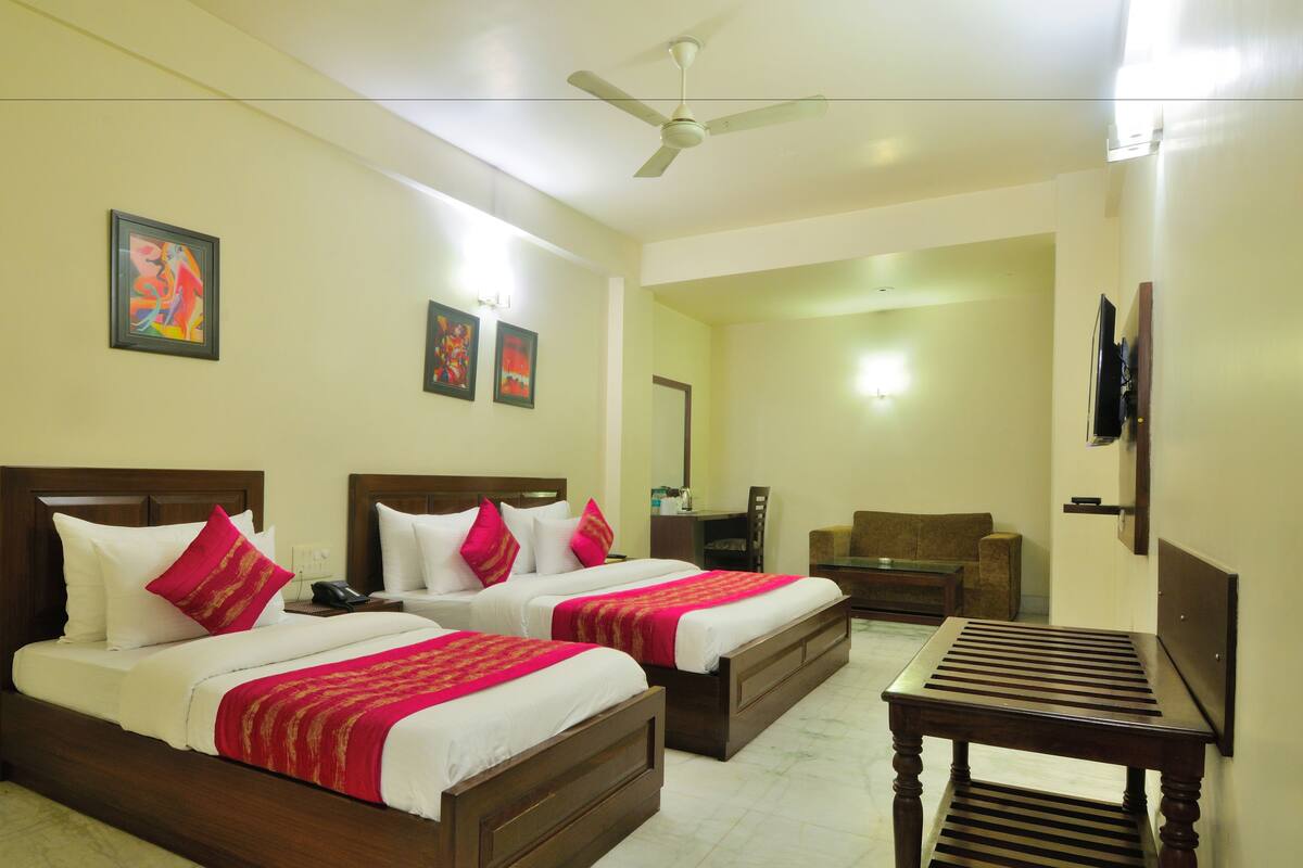 A hotel room with two beds, a desk, a chair, a TV, and artwork on the walls.