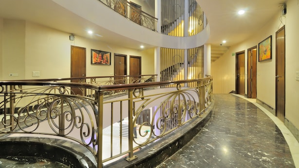 A multi-level hotel lobby with a curved marble floor, metal railings, and wooden doors. - Shanti Villa (New Delhi)