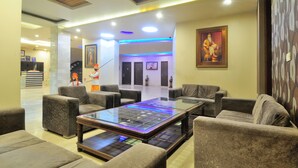 A lobby with a glass-top coffee table, sofas, and a reception area with a receptionist. - Shanti Villa (New Delhi)