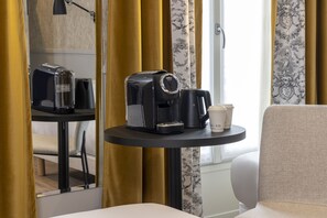 Una habitación de hotel con cafetera, una taza de café, una mesita y una silla.
