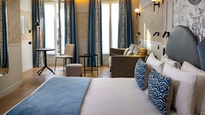 A hotel room with a large bed, a sitting area with a chair and a small table, and a large window with curtains. - Grand Hotel Leveque (Paris)