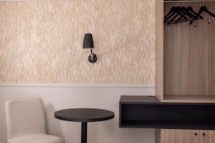 A modern room with a round table, a chair, a wall-mounted lamp, and a wooden wardrobe with hangers.