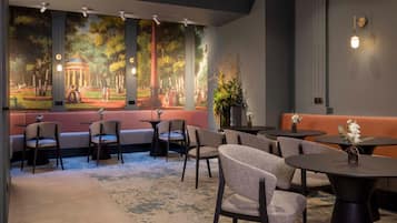 A restaurant with a mural of a garden scene, cushioned seating, and tables with small plants.