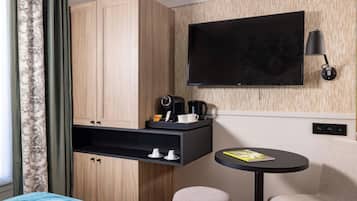 Una habitación de hotel moderna con una cama, un escritorio con cafetera, un televisor y una pequeña mesa con una revista.