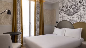 A hotel room with a bed, a chair, a small table, and a wall with a decorative pattern.
