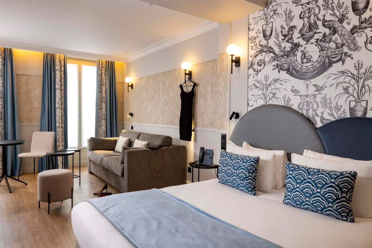 A hotel room with a bed, a sofa, a chair, a small table, and a wall-mounted phone.
