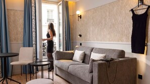 A modern living room with a grey sofa, a small round table, a chair, and a hanging dress. - Grand Hotel Leveque (Paris)