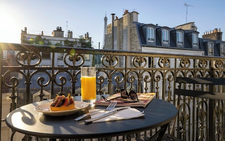 A balcony with a table set for a meal, including a plate of food, a glass of orange juice, and a pair of sunglasses.