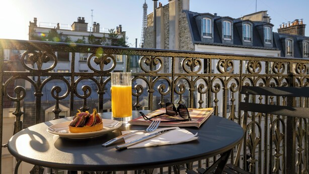 A balcony with a table set for a meal, including a plate of food, a glass of orange juice, and a pair of sunglasses. - Grand Hotel Leveque (Paris)