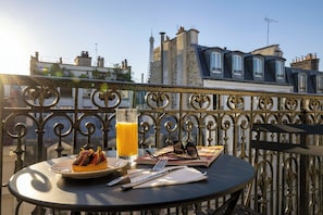 A balcony with a table set for a meal, including a plate of food, a glass of orange juice, and a pair of sunglasses. - Grand Hotel Leveque (Paris)