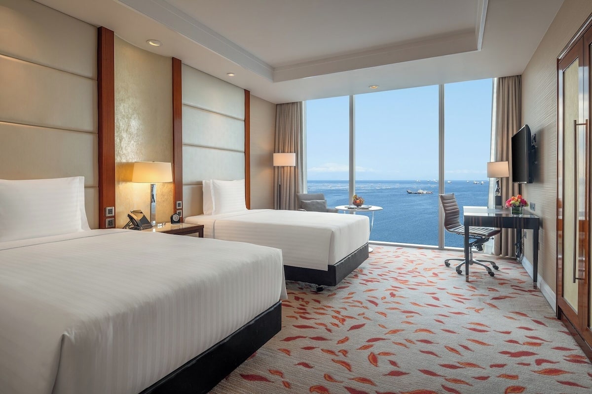 Une chambre d’hôtel avec deux lits, un bureau et une grande fenêtre donnant sur la mer.
