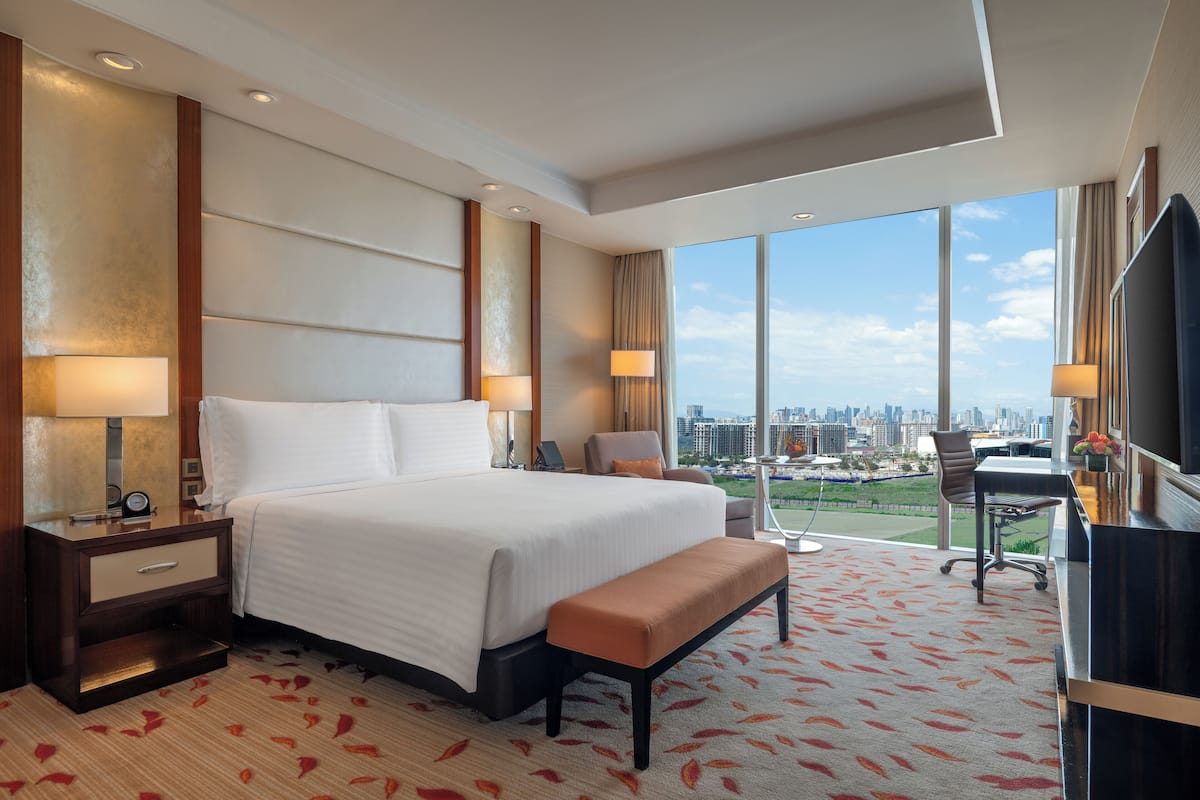 Une chambre d’hôtel avec un grand lit, un bureau, une chaise, une télévision et une vue sur la ville.