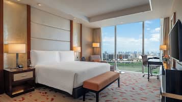 A hotel room with a large bed, a desk, a chair, a television, and a view of the city.