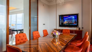 A conference room with a large wooden table, six orange chairs, and a television screen displaying a hotel view.