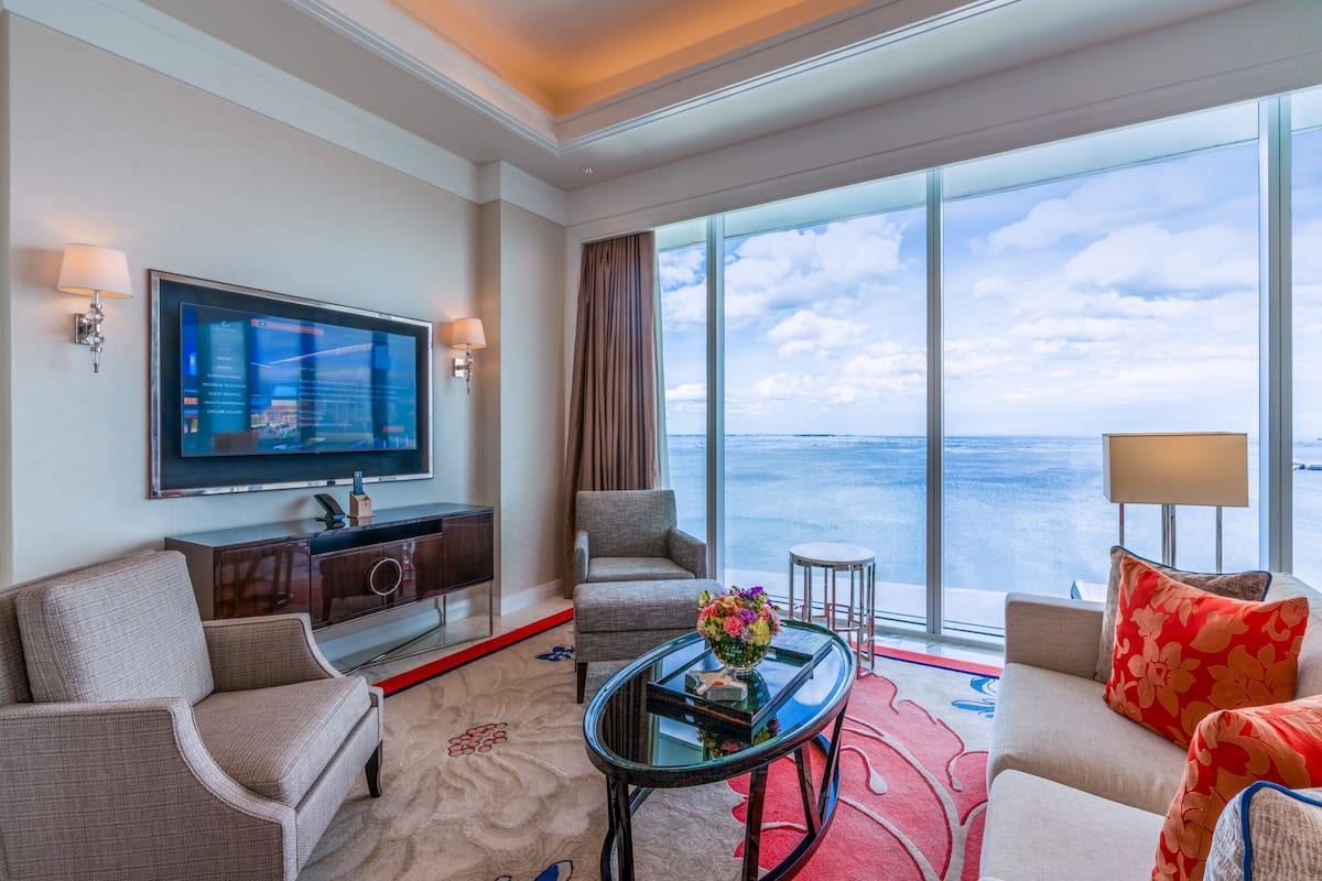 Une chambre d’hôtel dotée d’une grande télévision, de fauteuils confortables, d’une table basse en verre et offrant une vue sur la mer.