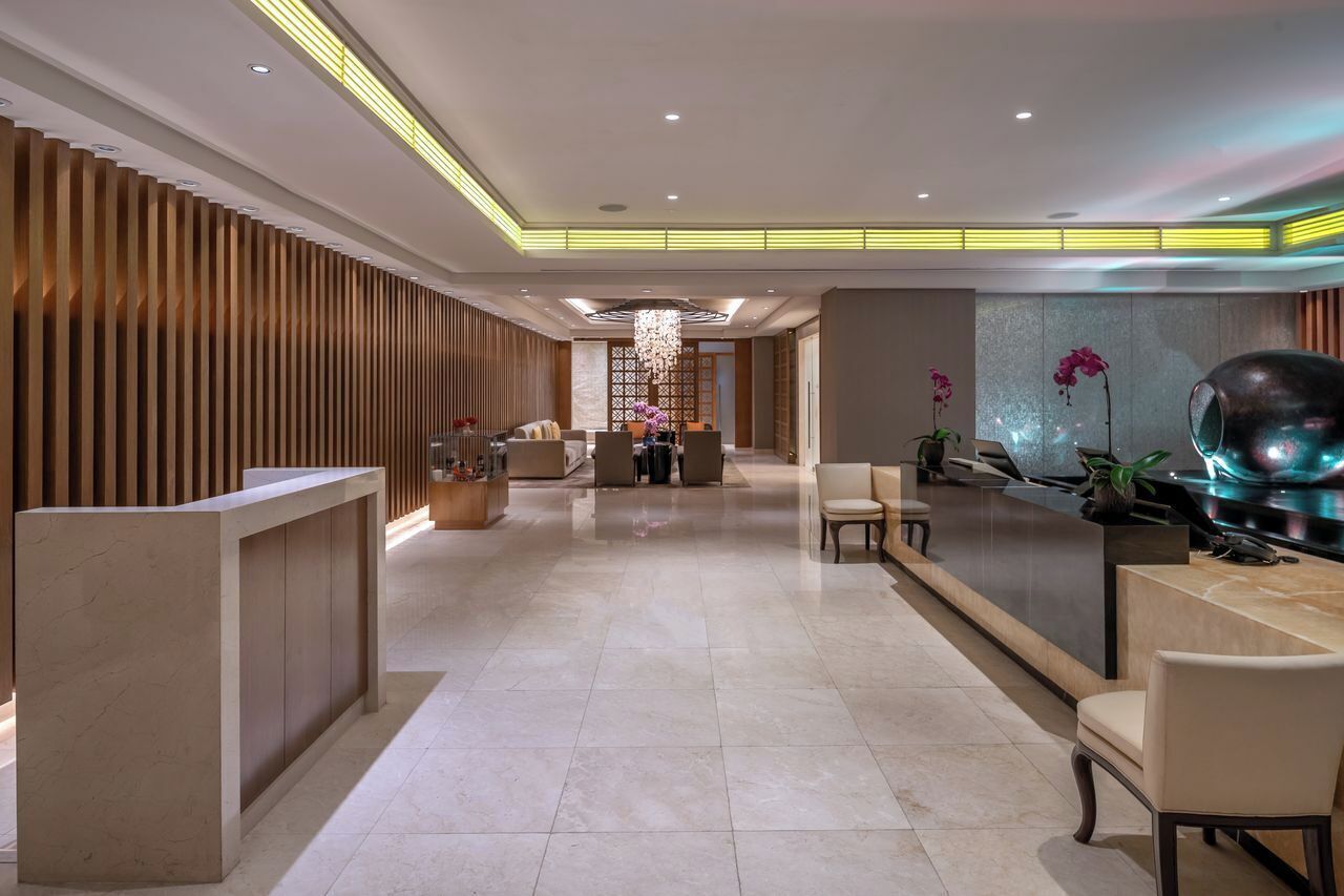 A modern hotel lobby with a reception desk, seating area, and decorative elements like orchids and a unique sculpture.