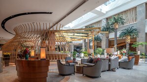 A spacious lobby with a modern design, featuring a central wooden structure, comfortable seating areas, and a high ceiling with skylights.